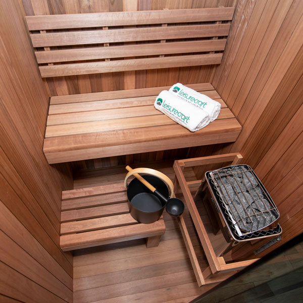 An inside view of the Dundalk CT Element Nook Indoor Sauna Kit. A stylish wooden indoor Sauna, 100% North American made. This image shows the tiered benches and electric heater.