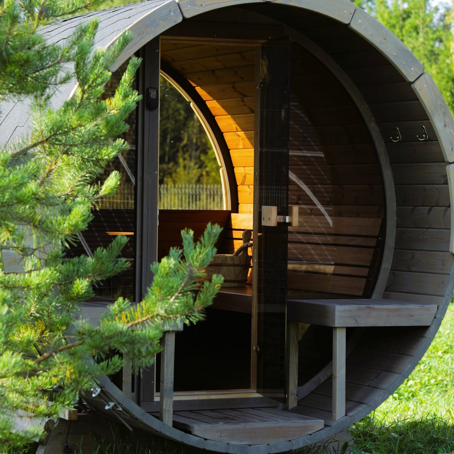 SaunaLife Outdoor Barrel Sauna with Glass Front - Positioned in a forest in the morning sun